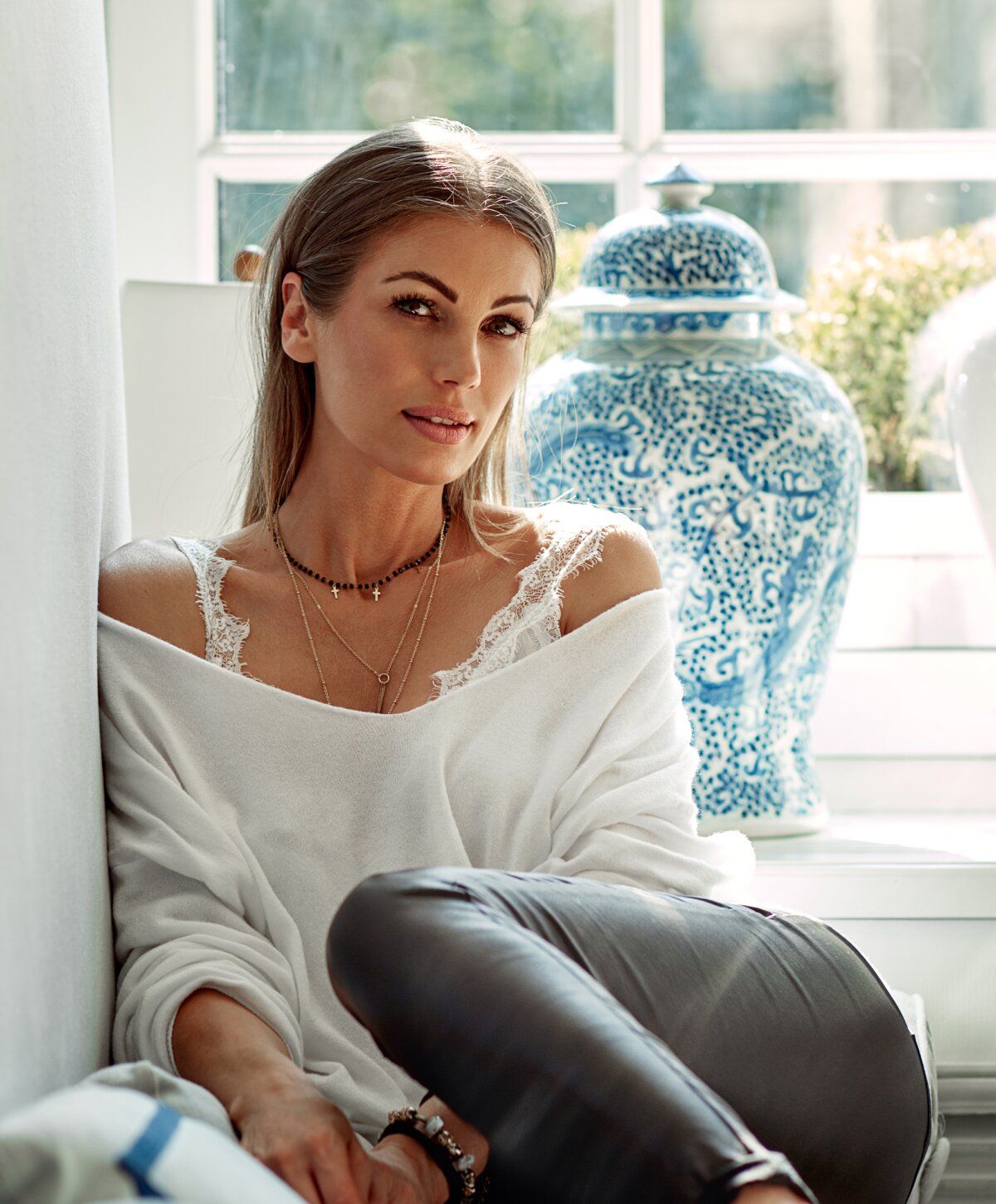 Woman relaxed by window with decorative vase.