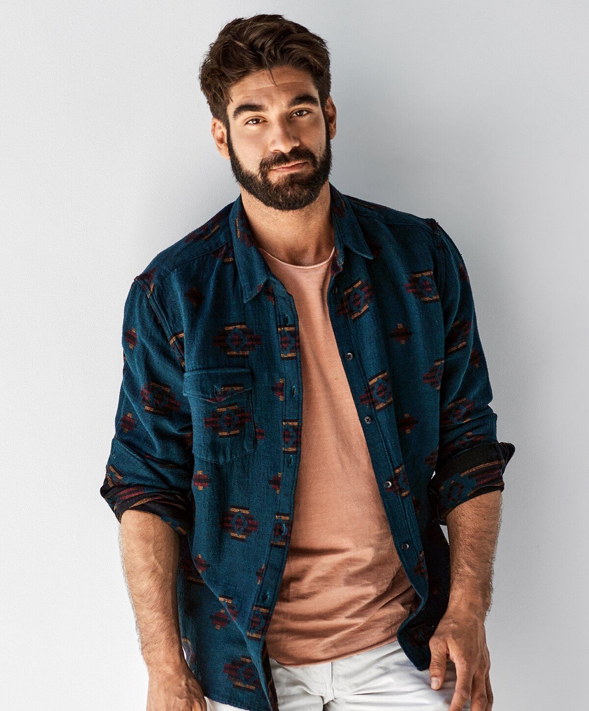 Man posing in stylish casual outfit against wall.