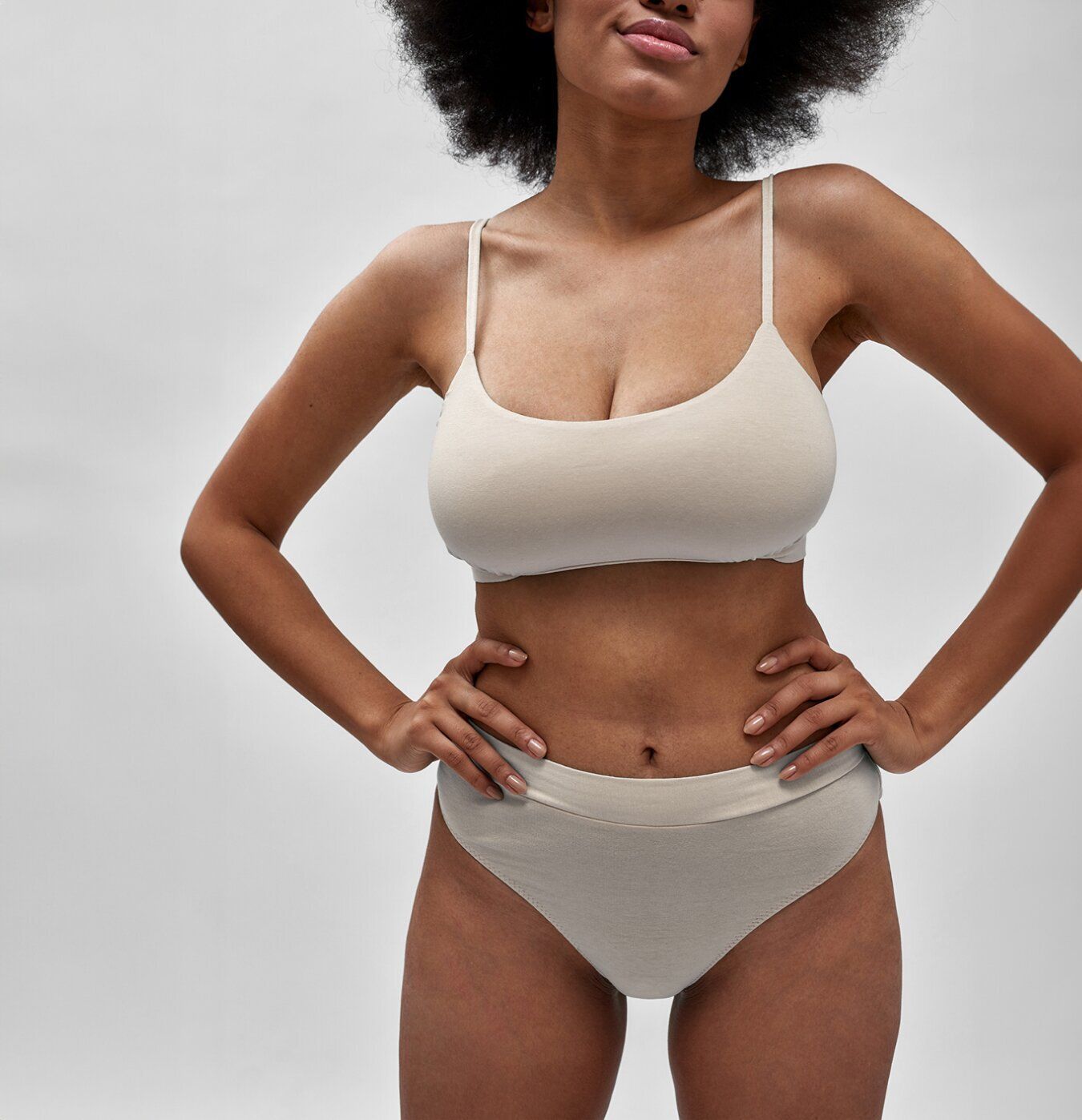 Model in beige lingerie with hands on hips.