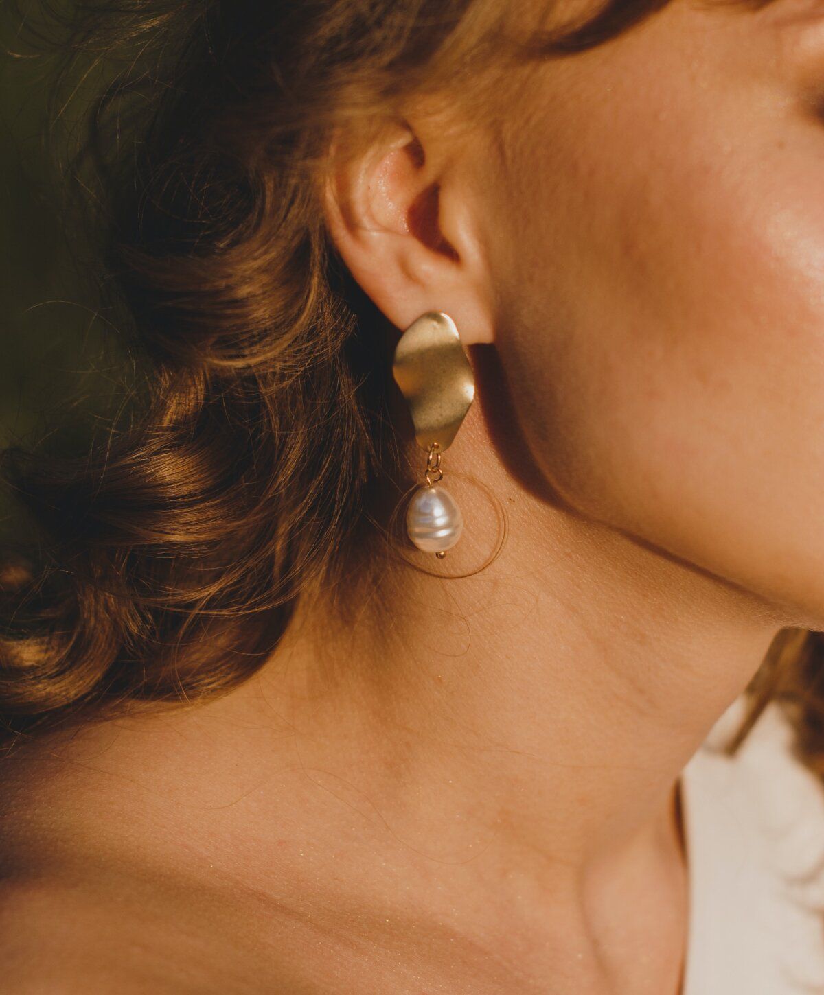 Gold earrings with pearl accent on model's ear.