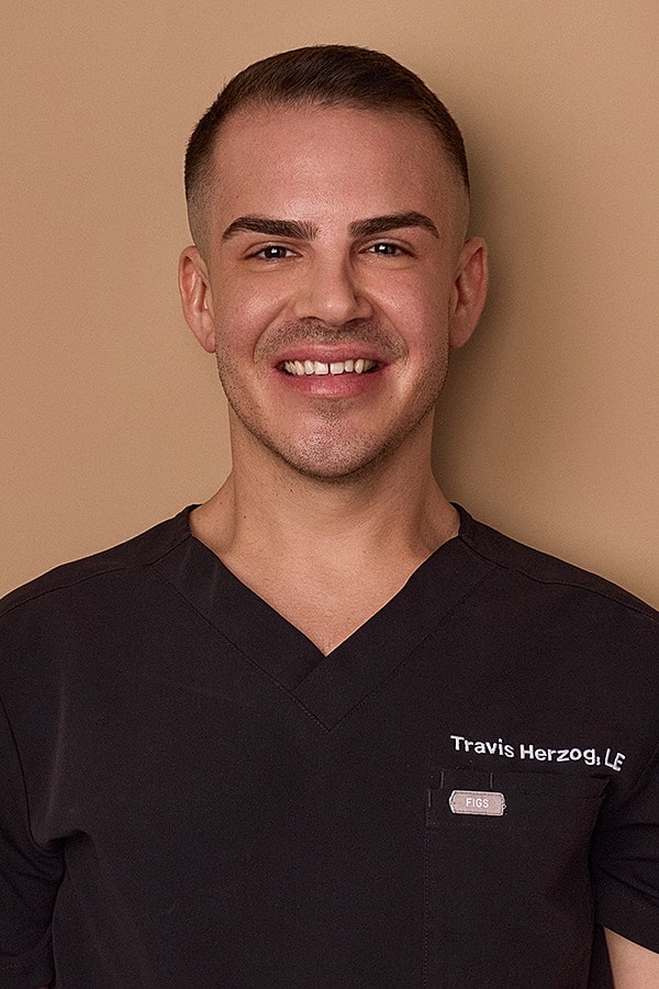 Smiling person wearing a dark medical uniform.