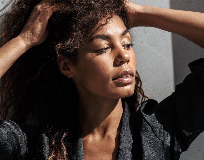 Woman with curly hair, sunlight, serene expression.