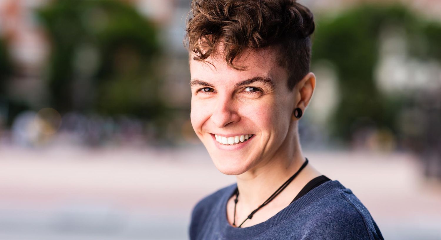 Smiling person with short, curly hair outdoors.